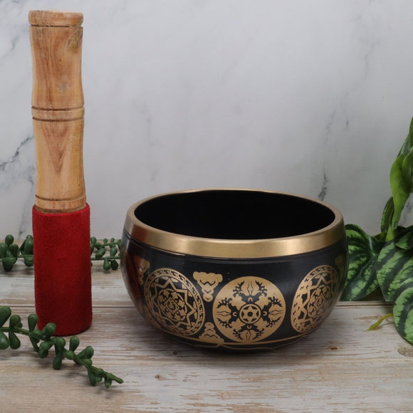 Decorative singing bowl with gold patterns on a wooden surface with a white marble background