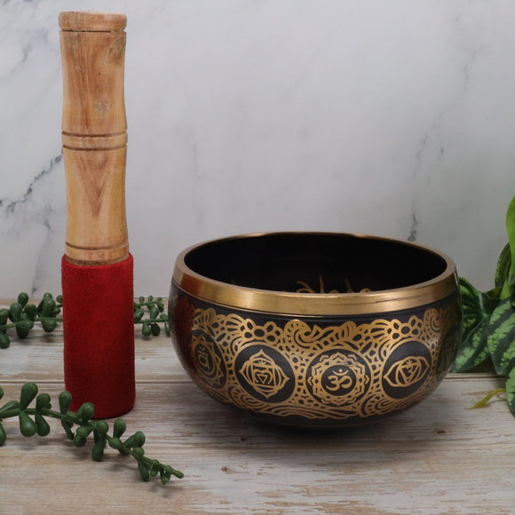 Decorative gold and black singing bowl with wooden striker on a marble surface
