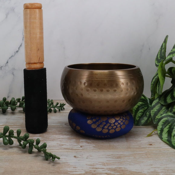Bronze singing bowl with wooden handle on a wooden surface with plants