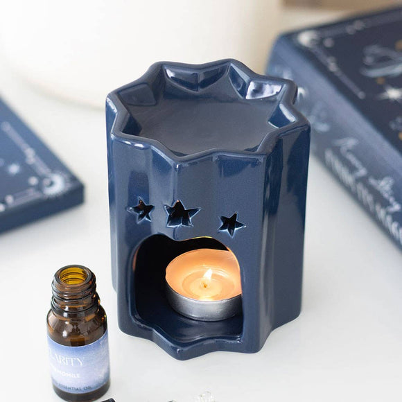 Navy blue star-shaped ceramic diffuser with a lit candle and a bottle of essential oil on a white surface.