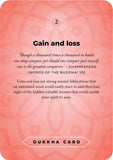 A single card from the Dukkha Card deck with a coral pink background and rounded corners. The card features black text titled 'Gain and loss' with a quote from the Buddha, the number 2 at the top, and 'DUKKHA CARD' printed inside a white label at the bottom.