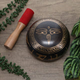 Decorative black and gold bell with a red mallet on a wooden surface with green leaves.