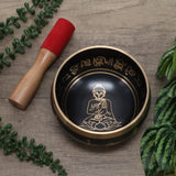Tibetan singing bowl with Buddha illustration on a wooden surface with leaves
