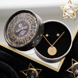 Gold necklace and earrings set in an 'Astrology' themed box on a reflective surface.
