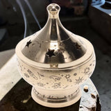 Decorative silver incense burner with star and moon designs on a dark surface.