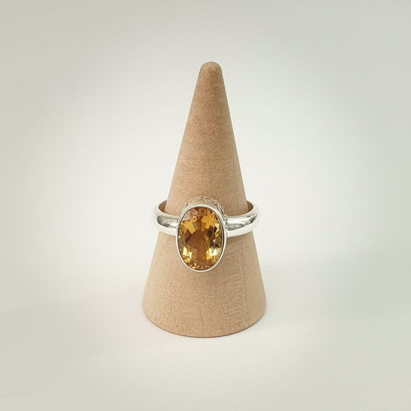 Silver ring with a yellow gemstone on a cardboard cone against a white background