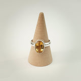 Silver ring with a yellow gemstone on a cardboard cone against a white background