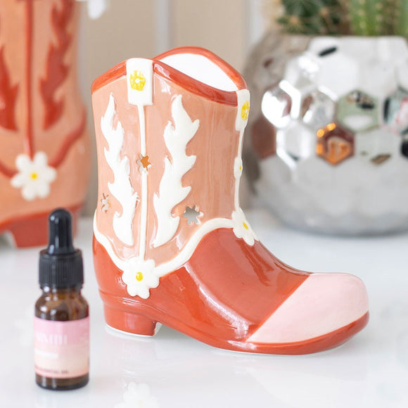 Decorative boot with floral patterns next to a small bottle on a light surface. Oil burner