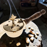Decorative incense holder with wooden handle and intricate design on a stone surface.