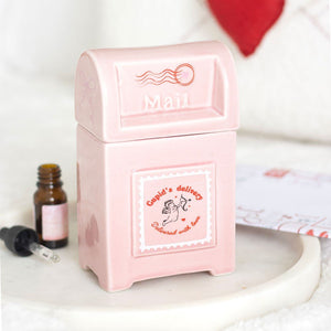 Pink mailbox-shaped container with 'Mail' text, next to a small bottle and dropper on a white surface.