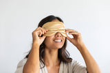 Woman wearing a gold satin sleep mask against a white background