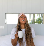 Woman with a pink headscarf holding a white mug in a bright room.