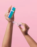 Hand holding a small bottle labeled 'Dreams' with a pink cap against a pink background