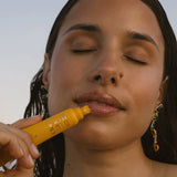 Woman applying a yellow lip balm with a scenic background