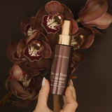 Hand holding a bottle of 'Super Fruit Essence' by Sonya against a dark background with flowers.