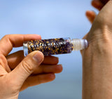 Roll-on bottle labeled 'Crystal Healing' held by a hand against a blue background