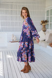 Woman wearing a floral dress standing on a wooden deck.