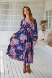 Woman wearing a floral dress standing on a wooden deck.