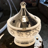 Decorative silver incense burner with star and sun designs on a wooden surface.