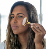 Woman using a gold facial roller on her face with a blurred background