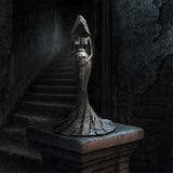 Gothic-style sculpture of a woman with a skull for a head on a dark staircase.