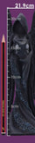 A tall, narrow product photo of a dark hooded winged figurine or statue with skull-like face details, shown against a purple background with a ruler scale and pencil on the left. White text overlays indicate measurements up to 21.