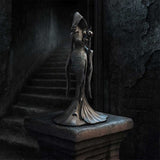 Statue of a hooded figure holding a lantern in a dark, stone-walled room.