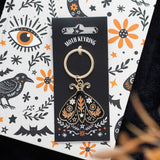 Moth keyring on a decorative card with floral and eye designs.
