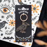 Raven keychain on a decorative card with Halloween-themed illustrations