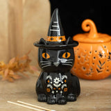 Black cat figurine with a witch hat on a wooden surface with a pumpkin in the background.