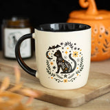 Mug with a cat design on a wooden surface with a candle and pumpkin in the background