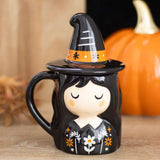 Halloween-themed mug with witch design and black hat on a wooden surface.