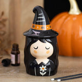 Decorative witch figurine with a pumpkin and bottle in the background
