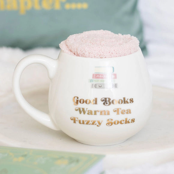 White mug with text 'Good Books Warm Tea Fuzzy Socks' and pink fluffy top on a light background