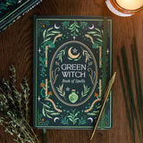 Book titled 'Green Witch Book of Spells' on a wooden surface with herbs and candles.