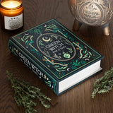 Decorative book titled 'Green Witch Book of Spells' on a wooden surface with a candle and decorative ball.