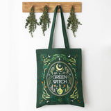 Green tote bag with 'Green Witch' design hanging on a wooden hook against a white background