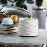 White ceramic planter with wavy texture on a table with decorative items in the background