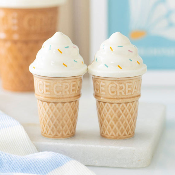 Two ice cream cone-shaped salt and pewith white cream and colorful sprinkles on a marble surface.per shakers 
