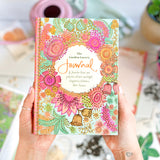 Colorful journal with floral design held by a person, surrounded by blurred garden-themed items.