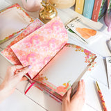 Floral notebook being opened on a desk with books and stationery items.