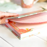Hand holding a colorful book with floral design on a white surface
