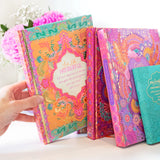 Colorful notebooks with floral designs and text held by a hand on a light background