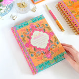 Colorful notebook with floral design on a white surface with office supplies.