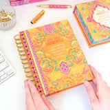 Colorful notebook with floral design and motivational quote on a desk with office supplies.