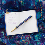 Blue pen with gold accents on a notebook with writing on a colorful fabric background