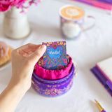 Hand holding a colorful card with 'Mindset' text over a stack of similar cards on a desk with a cup and flowers.