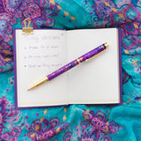 Open notebook with a purple pen on a colorful fabric background