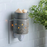 Decorative wall-mounted wax warmer with two wax melts on a tiled wall.