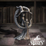 Statue of a witch with a cat on a stone floor with bookshelves in the background, featuring the brand 'Little Souls'.